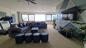 Un salon moderne avec un grand canapé d’angle, un tapis de course et un téléviseur à écran plat.