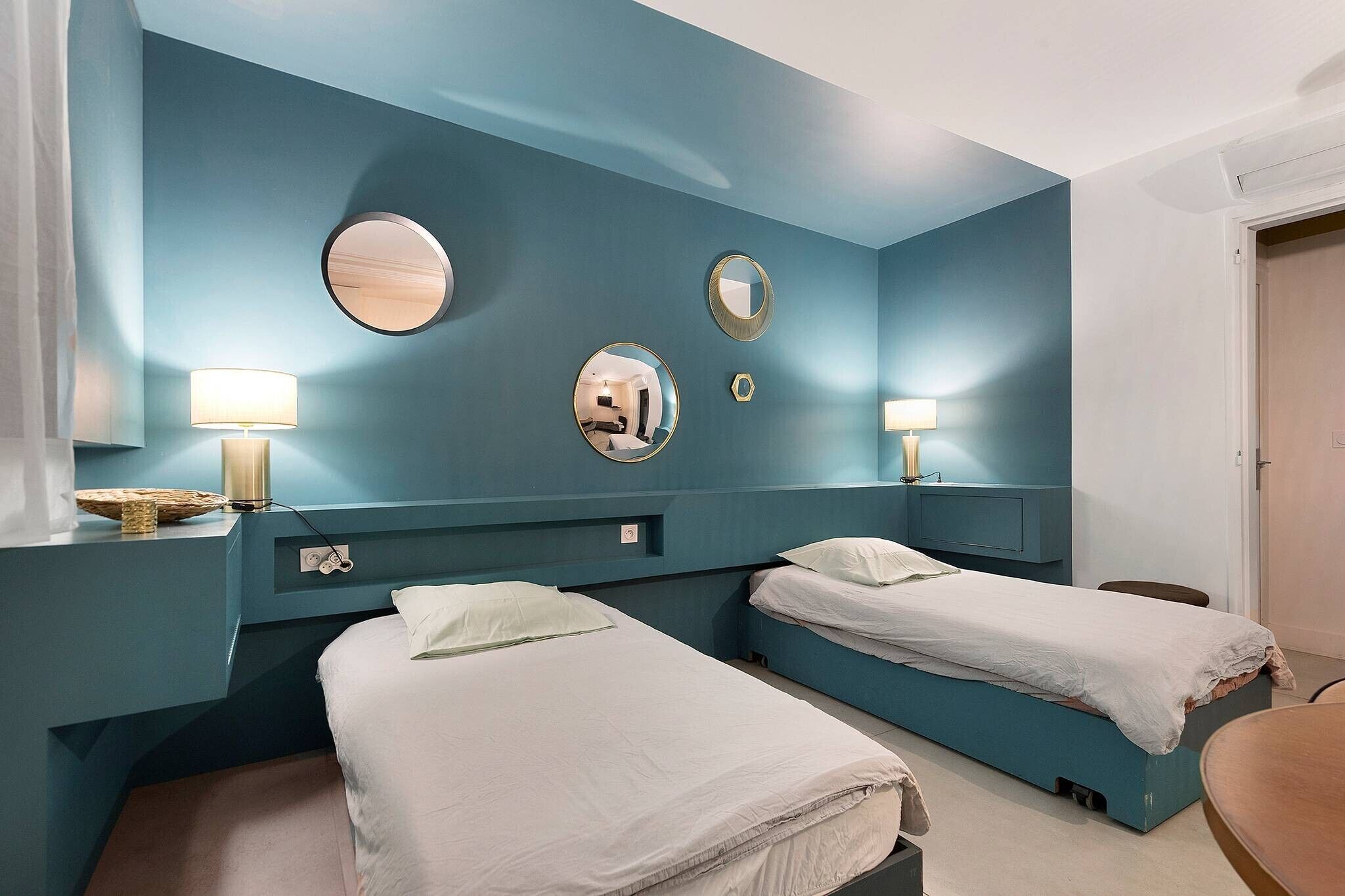 Une chambre avec deux lits, un miroir et une lampe fixée au mur.