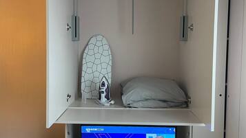 A compact room with a bed, a small table, and a TV displaying a news program.