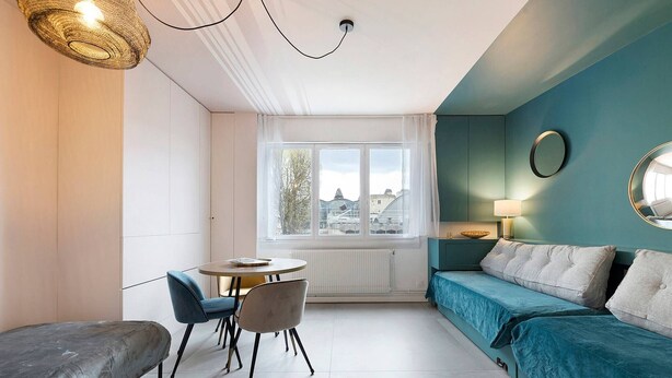 Ein Zimmer mit einer Couch, einem Esstisch mit Stühlen, einem Fenster mit Vorhängen und einer Lampe.