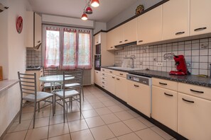 Une cuisine équipée d’une table à manger, de chaises, de placards, d’une cuisinière et d’une bouilloire rouge.