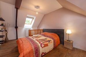 Une chambre avec un plafond en pente, un lit recouvert d’une couverture orange, une lampe de chevet, une petite fenêtre et une tête de lit en bois.