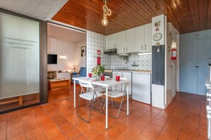 Een praktische keuken met witte kasten, een eettafel met stoelen, een kleine koelkast en een klok aan de muur.