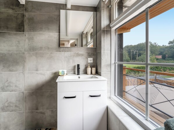 A bathroom with a white sink, a mirror, and a window with a view of a garden and trees.