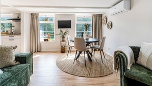 A spacious living area with a round dining table, two sofas, a TV, and a large window with curtains.