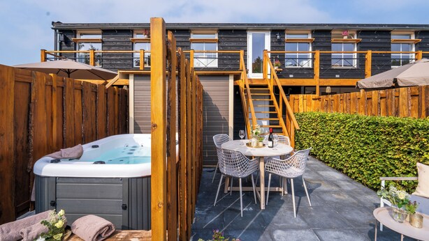 A wooden deck with a hot tub, outdoor seating, and a wooden fence.