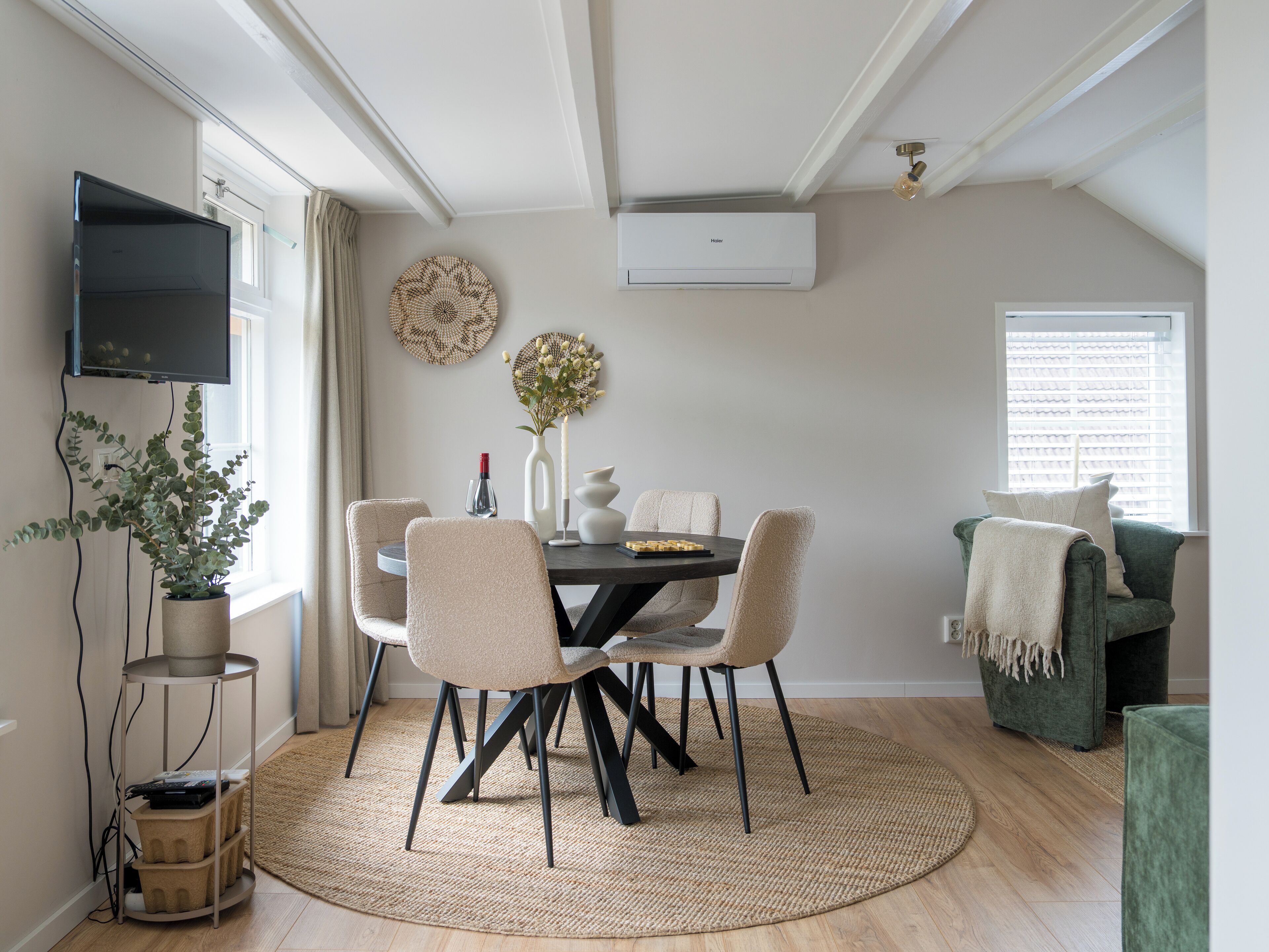 Un comedor con una mesa redonda, cuatro sillas, una planta en maceta y un aire acondicionado de pared.