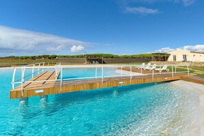 A swimming pool with a wooden deck, lounge chairs, and a building in the background.