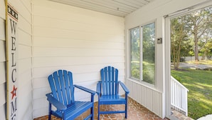 Un porche cubierto con dos sillas Adirondack azules y un letrero que dice 'WELCOME'.