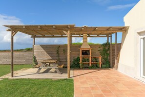A patio with a pergola, a brick oven, and a picnic table.