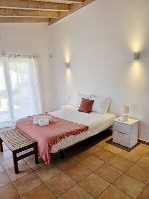 A bedroom with a bed, bedside table, lamp, and a bench.