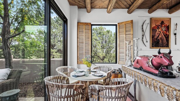 A dining area with wicker chairs, a round table, and a view of trees through large windows. - Stunning Views, Southwestern Elegance (Santa Fe)