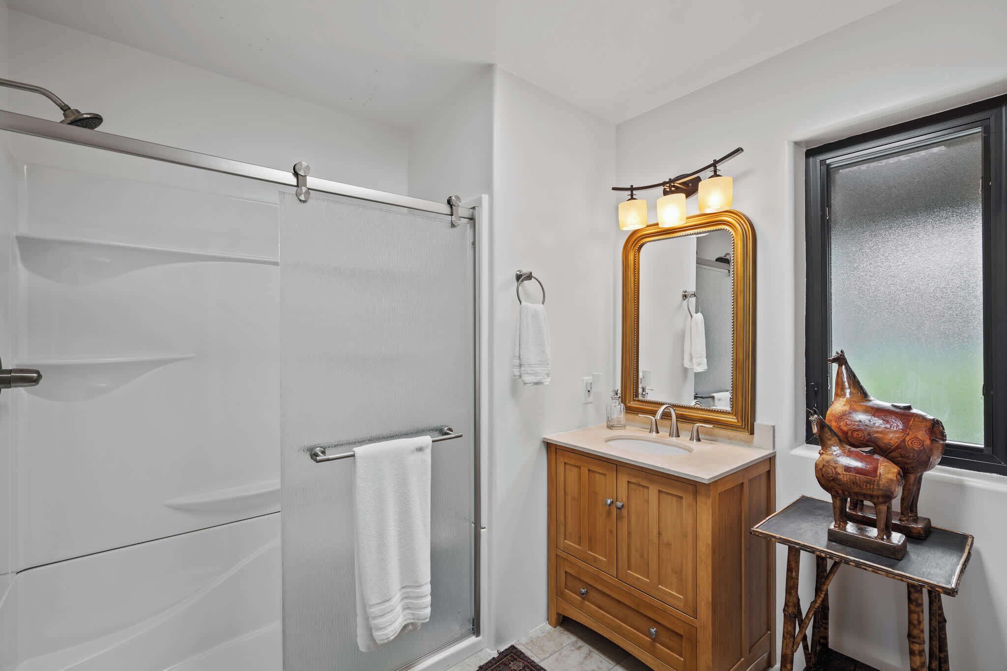 A bathroom with a walk-in shower, a wooden vanity with a mirror, and a decorative horse sculpture.