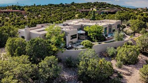 A modern villa with multiple levels, surrounded by lush greenery and a mountainous backdrop. - Stunning Views, Southwestern Elegance (Santa Fe)