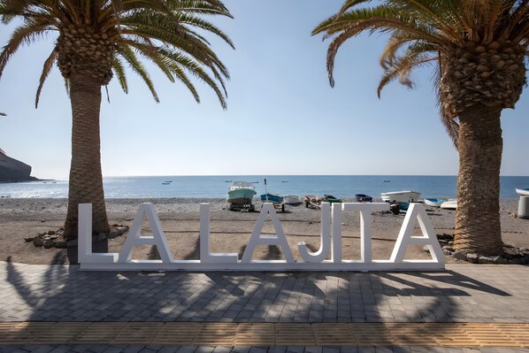 Une vue sur la plage, avec des palmiers, et le mot « LAJIA » au premier plan.