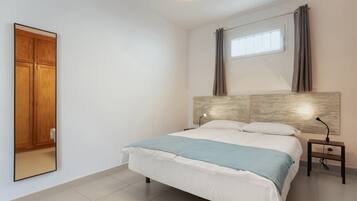 Um quarto com uma cama, uma mesa de cabeceira, um espelho, uma janela com cortinas e um guarda-roupa de madeira.
