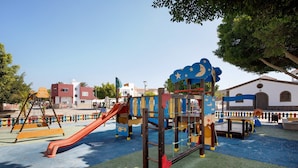Ein Spielplatz mit Rutschen und Klettergerüsten, umgeben von Gebäuden und Bäumen.