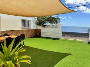 Une terrasse avec un revêtement de gazon synthétique, une table en bois, des chaises, une clôture blanche et une vue sur la mer.