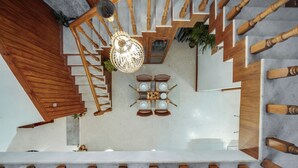A modern interior with a wooden staircase, a dining area with a table and chairs, and a hanging light fixture.