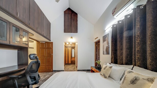 A hotel room with a large bed, a desk with a chair, wooden cabinets, a ceiling light, and a view of the hallway.