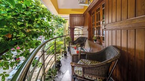 A balcony with wicker furniture, potted plants, and a view of the street below.