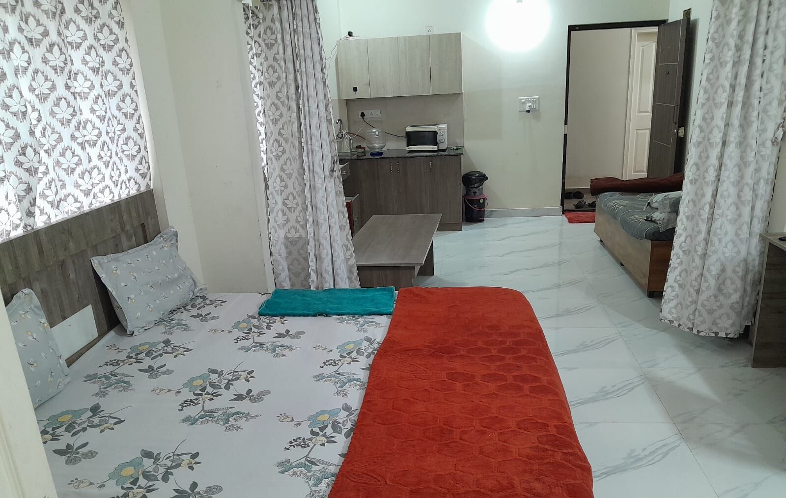 A bedroom with a bed, a small table, a microwave, and a wardrobe.