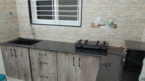 A kitchen with a black countertop, a sink, a stove, and wooden cabinets. - SAGAR NIWAS (Anekal)