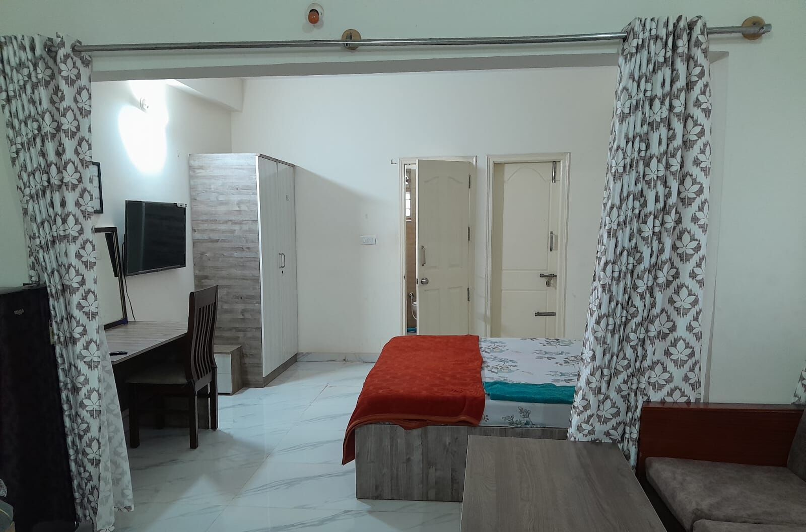 A bedroom with a bed, a desk, a chair, a wardrobe, and a television.