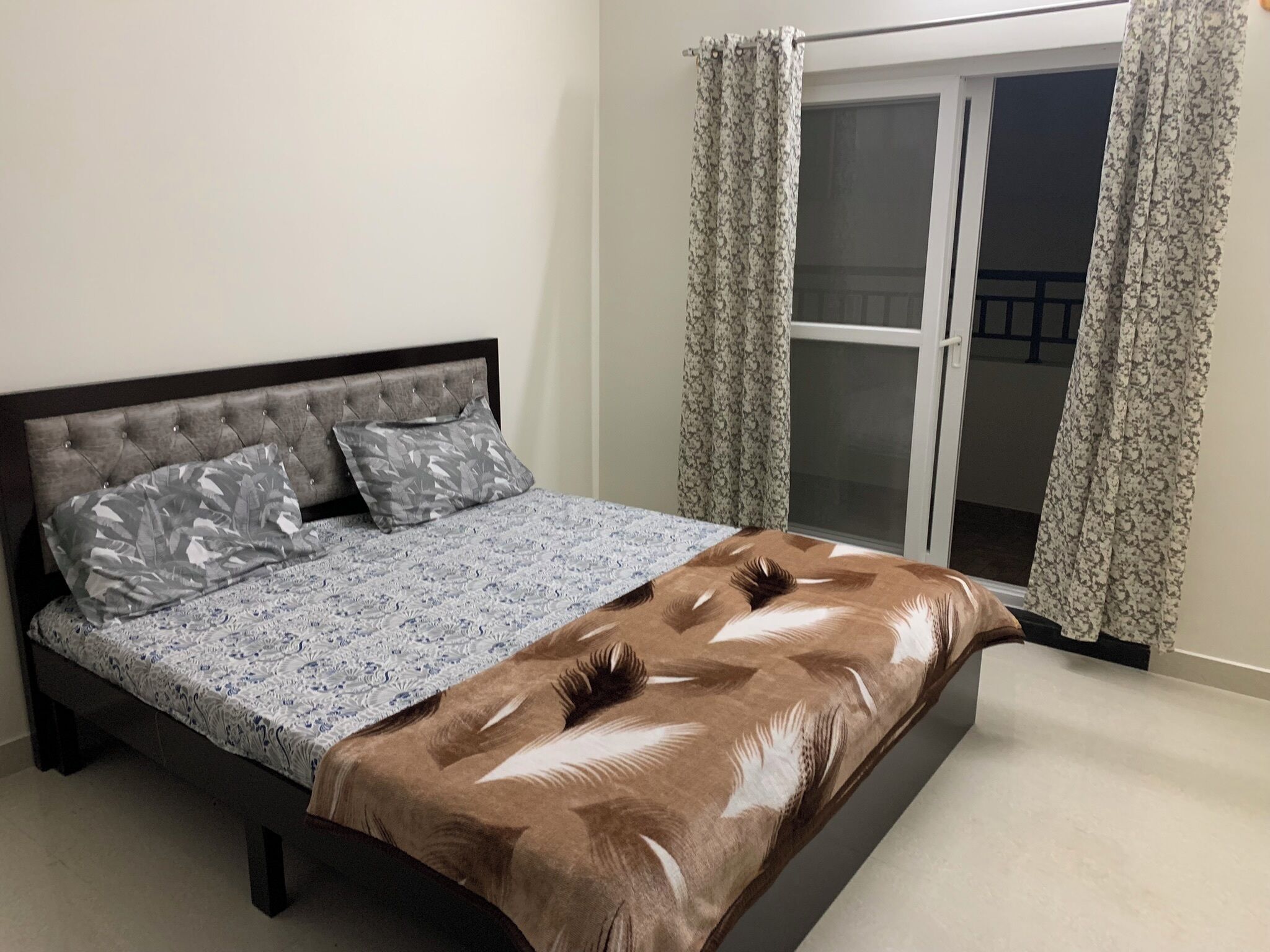 A bedroom with a bed, a window with curtains, and a balcony.