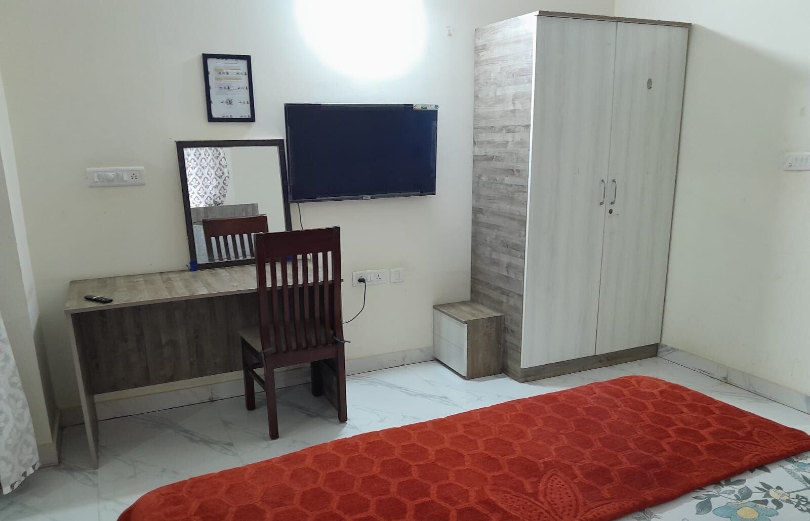 A bedroom with a bed, a desk, a chair, a wardrobe, and a television.