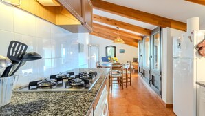 A kitchen with granite countertops, a gas stove, and wooden ceiling beams. - Country House 'Vinyoles 2' with Mountain View, Shared Pool and Wi-Fi (Quart)