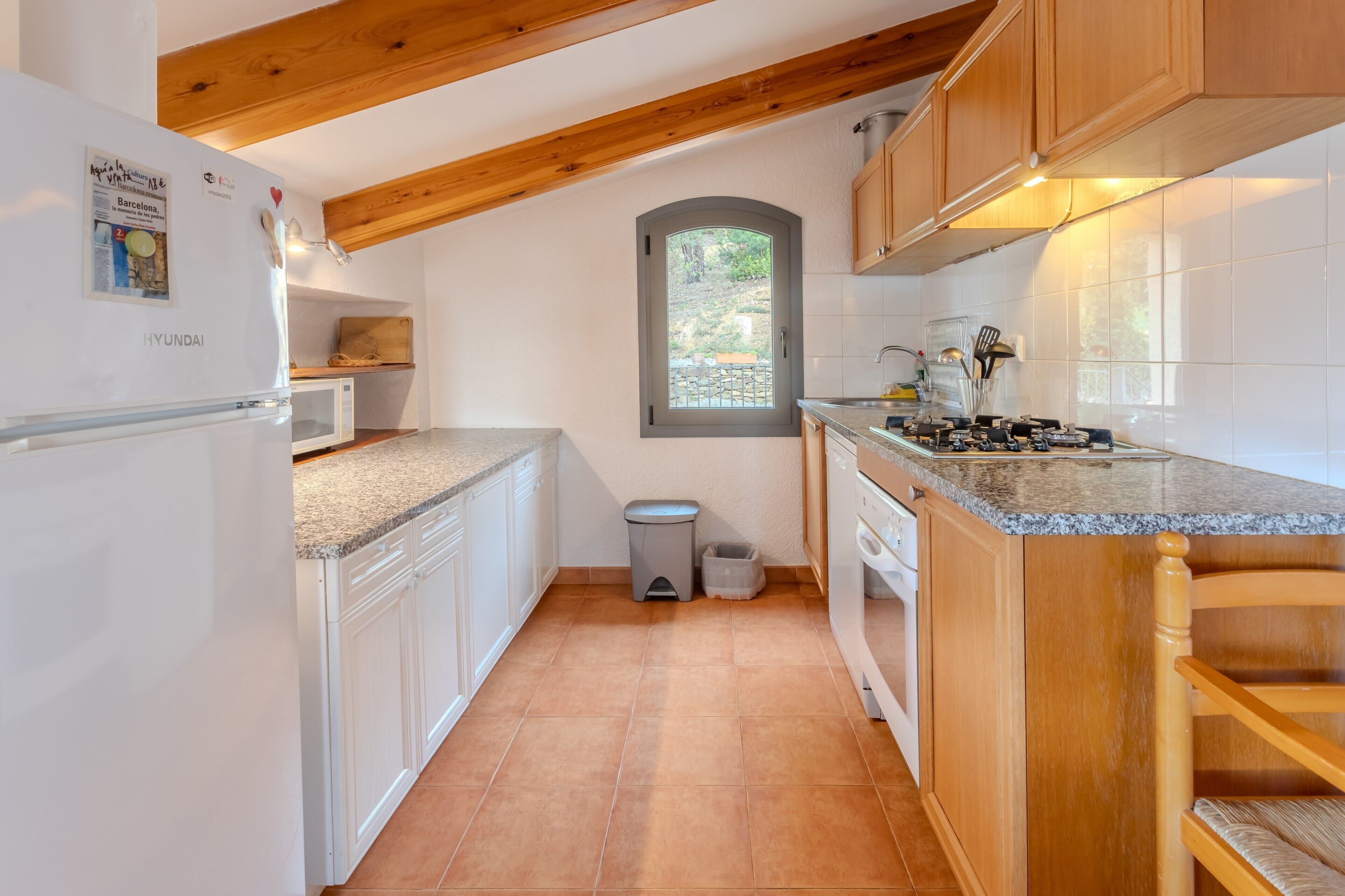 Una cocina con armarios blancos, encimera de granito, techo de madera y una ventana.
