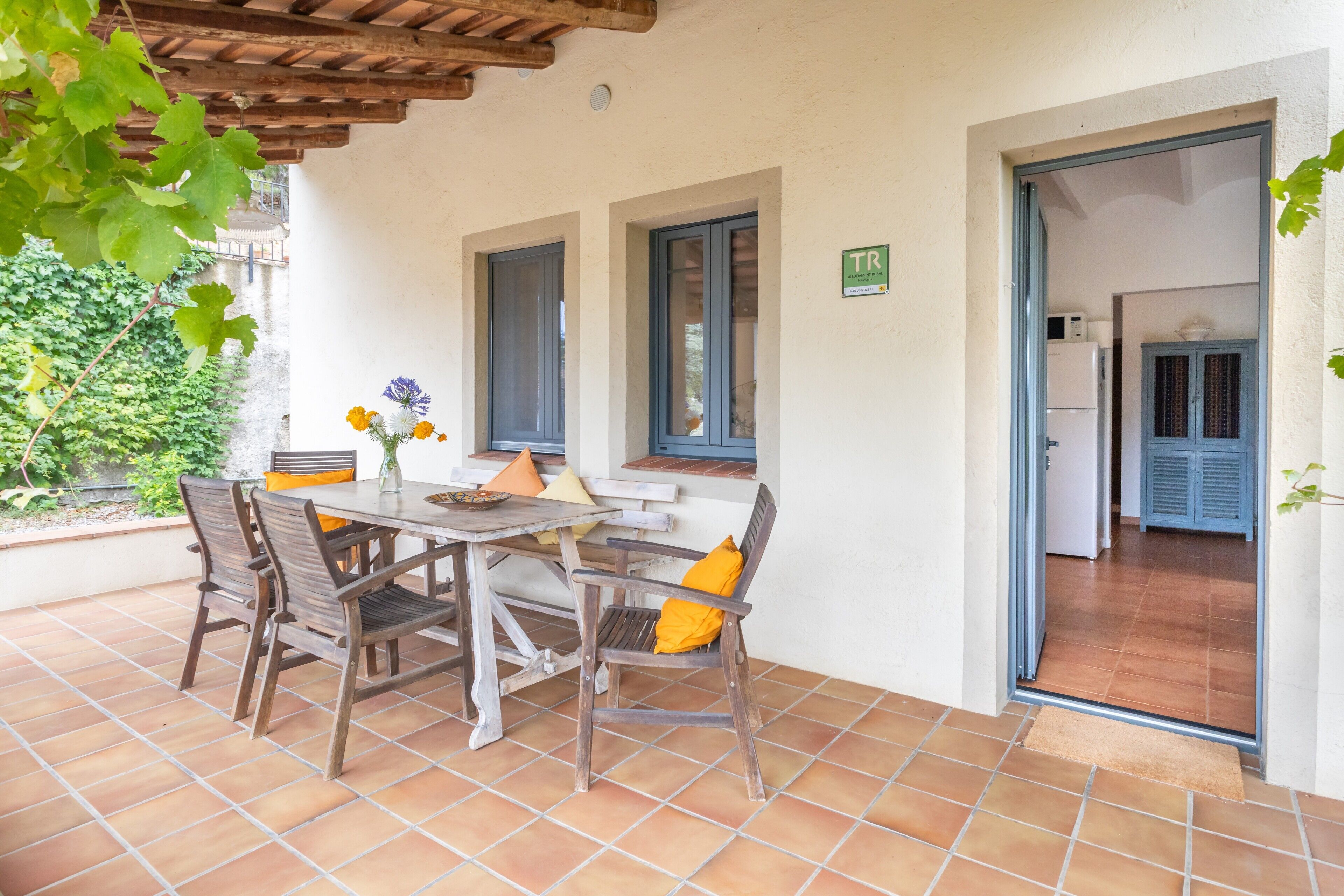 An outdoor patio with a table and chairs, a door leading to a kitchen, and a view of a building in the background.