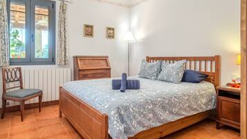 Ein Schlafzimmer mit einem hölzernen Bett, einem Sessel, einem Nachttisch, einer Lampe und einem Fenster mit Vorhängen.