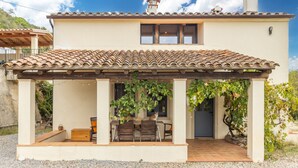 A house with a tiled roof, a covered patio with a table and chairs, and a cat sitting on the patio. - Rural House 'Vinyoles 1' with Mountain View, Shared Pool and Wi-Fi (Quart)
