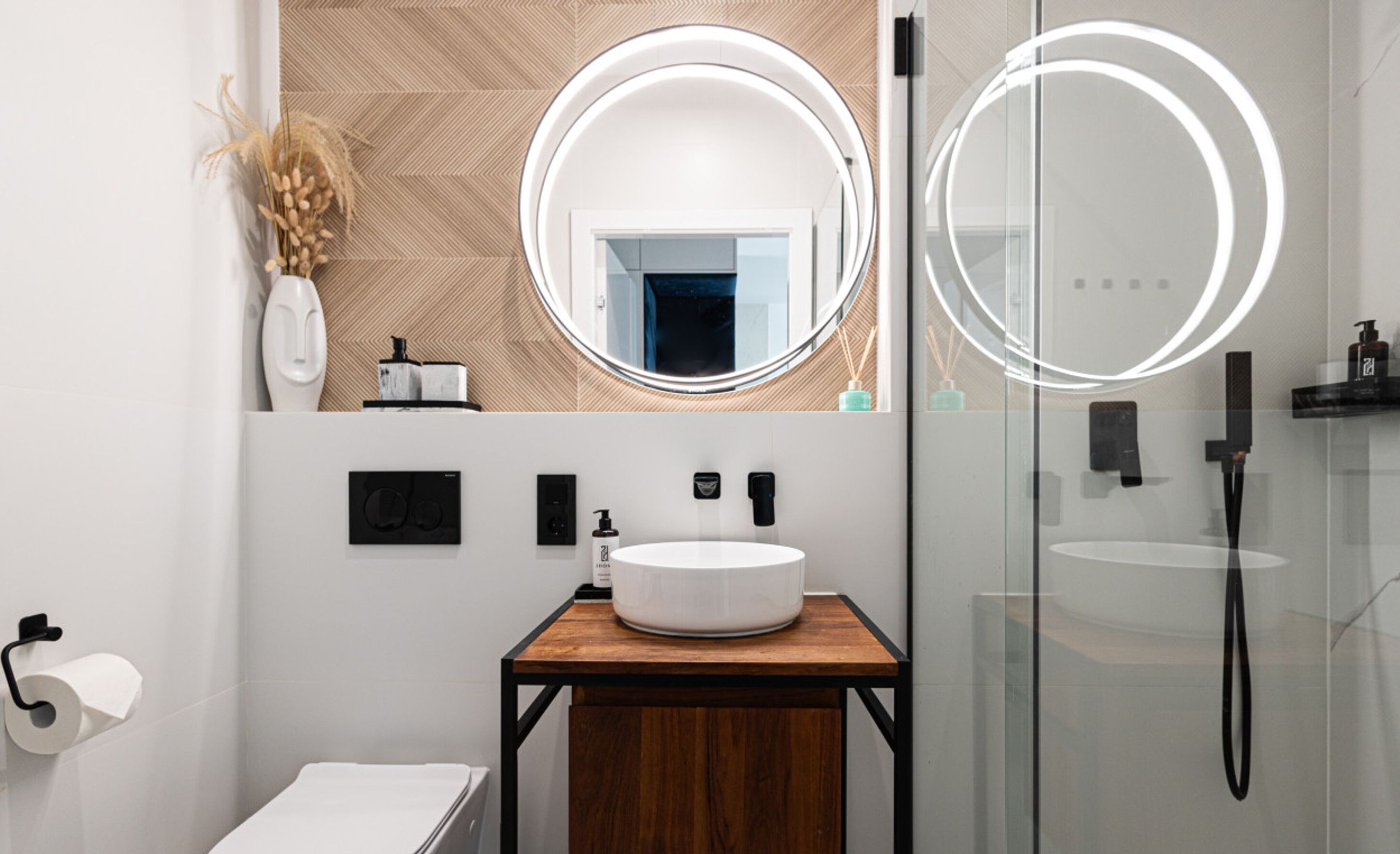 Une salle de bain moderne avec un grand miroir rond, un meuble-lavabo en bois, un lavabo blanc et une cabine de douche en verre.