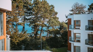 Un edificio moderno con balcones que dan a un cuerpo de agua y árboles frondosos.