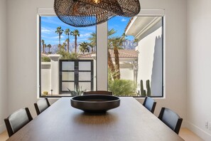 A dining area with a long table, chairs, and a hanging light fixture. - Via Elegante -Designer Home in Rancho Mirage, Pool, Spa, BBQ. Mountain View (Rancho Mirage)