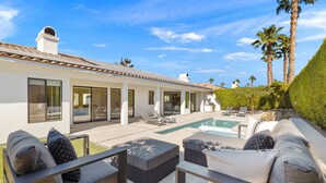 A modern house with a pool, outdoor seating, and palm trees.