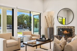 A modern living room with a fireplace, comfortable seating, and a view of the outdoors. - Via Elegante -Designer Home in Rancho Mirage, Pool, Spa, BBQ. Mountain View (Rancho Mirage)