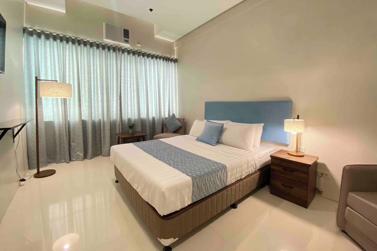 A modern hotel room with a large bed, a bedside table, a lamp, and a chair.