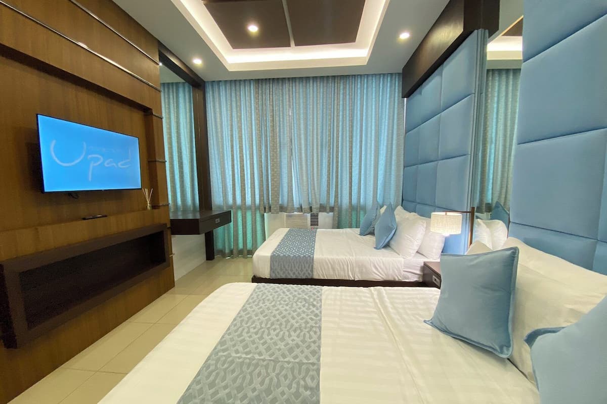 A modern hotel room with a large bed, a TV mounted on the wall, and a ceiling with recessed lighting.