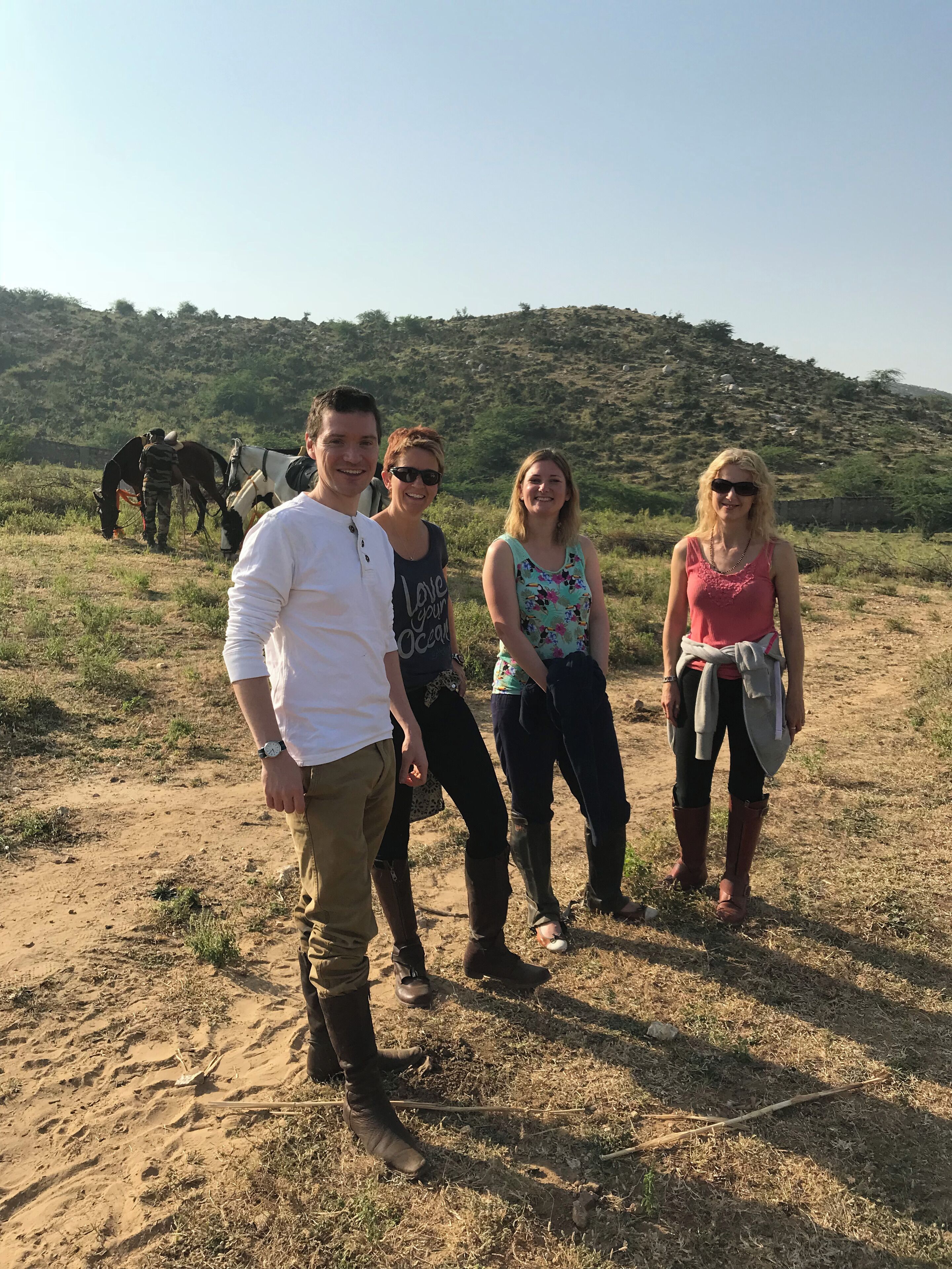 A group of people standing in a dry, grassy field with a hilly landscape in the background.
