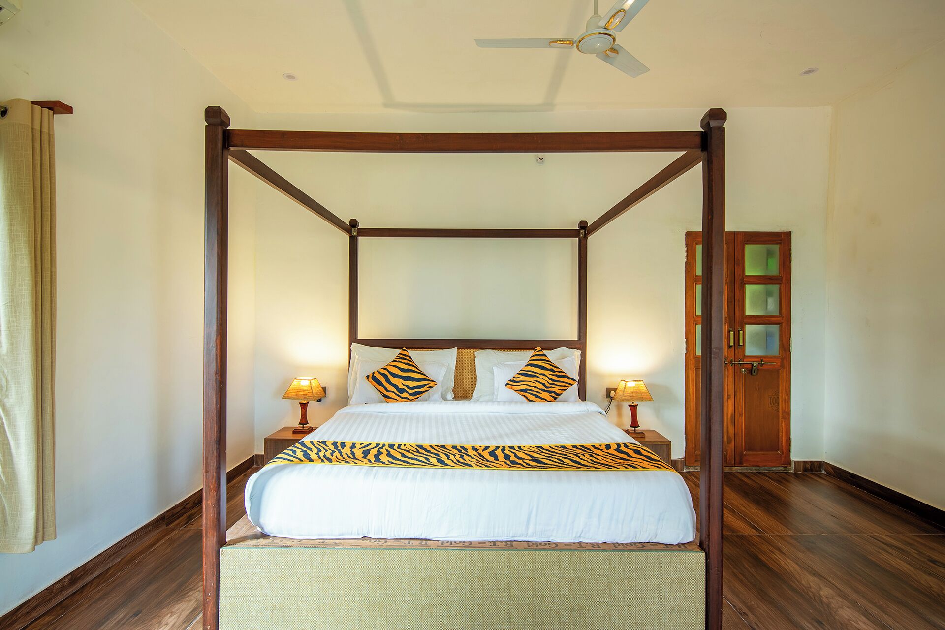 A four-poster bed with a canopy, two bedside lamps, and a wooden door with frosted glass panels.