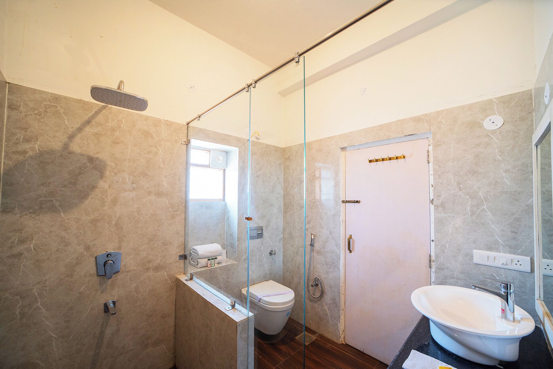 Egy modern fürőszoba üvegfalas zuhanyzóval, WC-vel és mosdókagylóval, melynek felett tükör található.