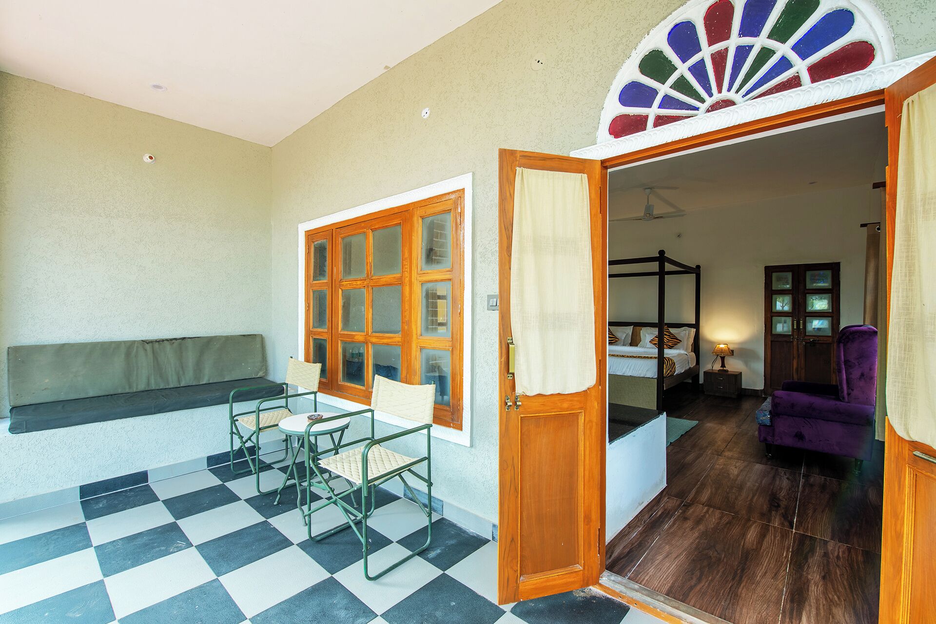 Een kamer met een zwart-wit geruite vloer, een houten deur, een bed, een paarse stoel en een raam met decoratieve details.