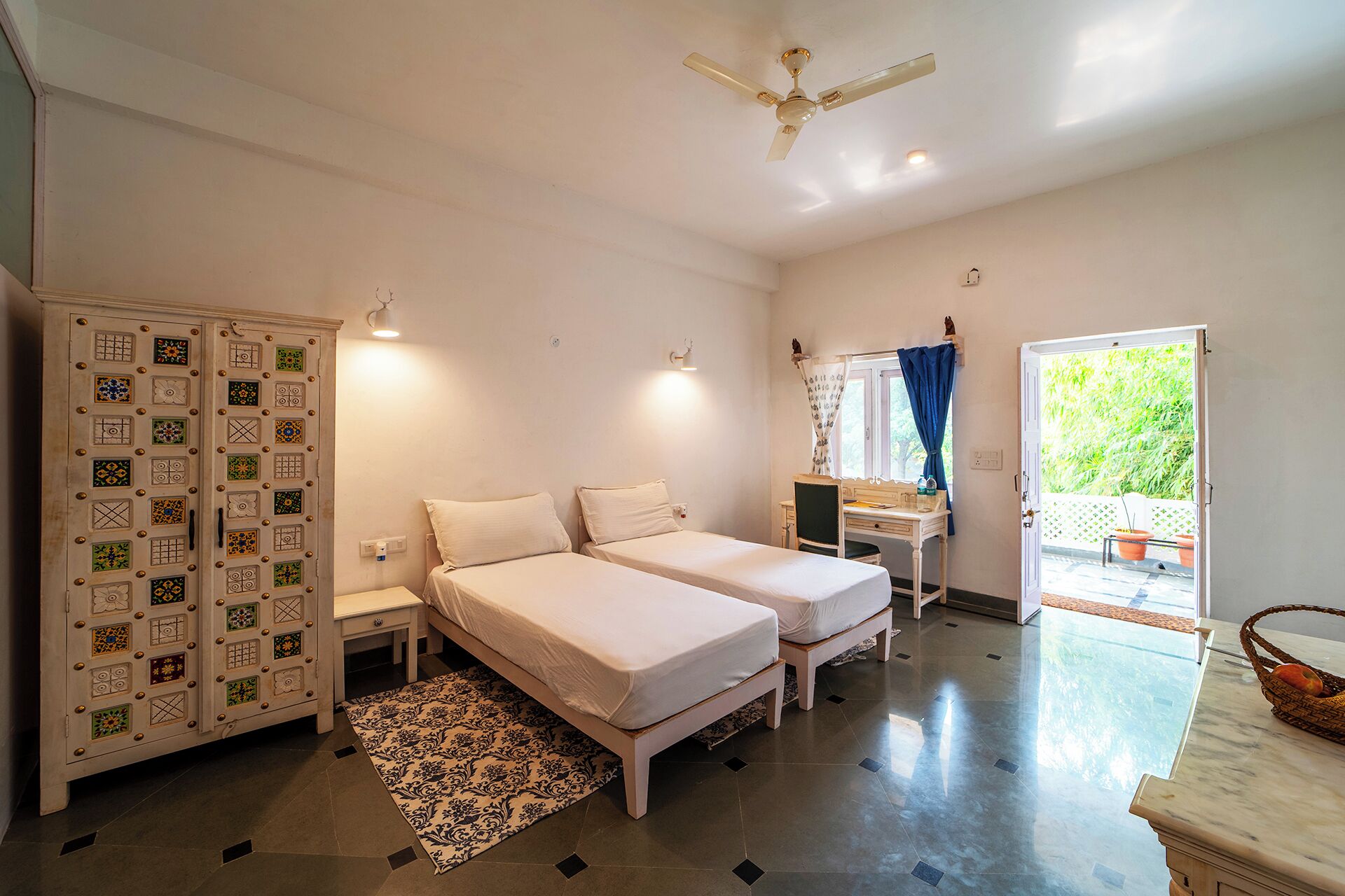 A bedroom with two beds, a desk, a wardrobe, and a ceiling fan.
