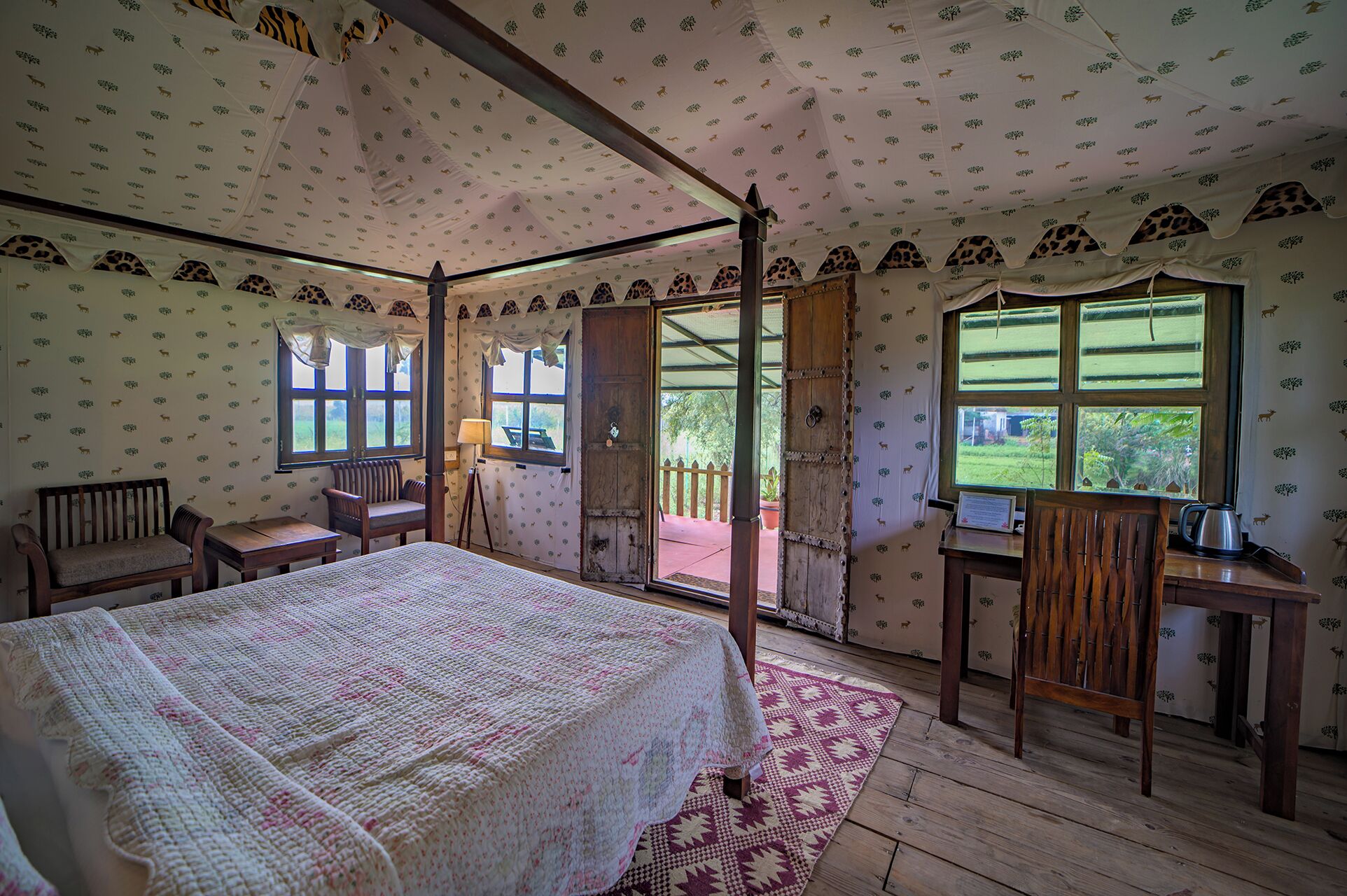 Un lit à baldaquin avec une couvre-lit à motifs, un bureau en bois avec une chaise, et une vue sur l’extérieur grâce à une grande fenêtre.