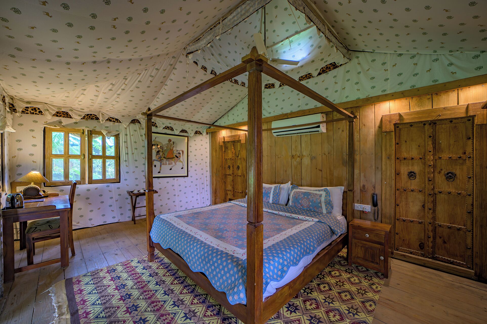 A four-poster canopy bed with a patterned bedspread, wooden walls, and a patterned rug.