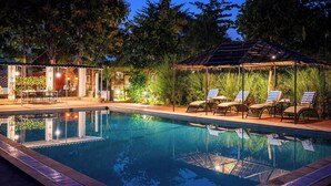 A swimming pool with lounge chairs and a covered seating area, surrounded by trees and vegetation. - Maa Ashapura Resort (Sawai Madhopur)